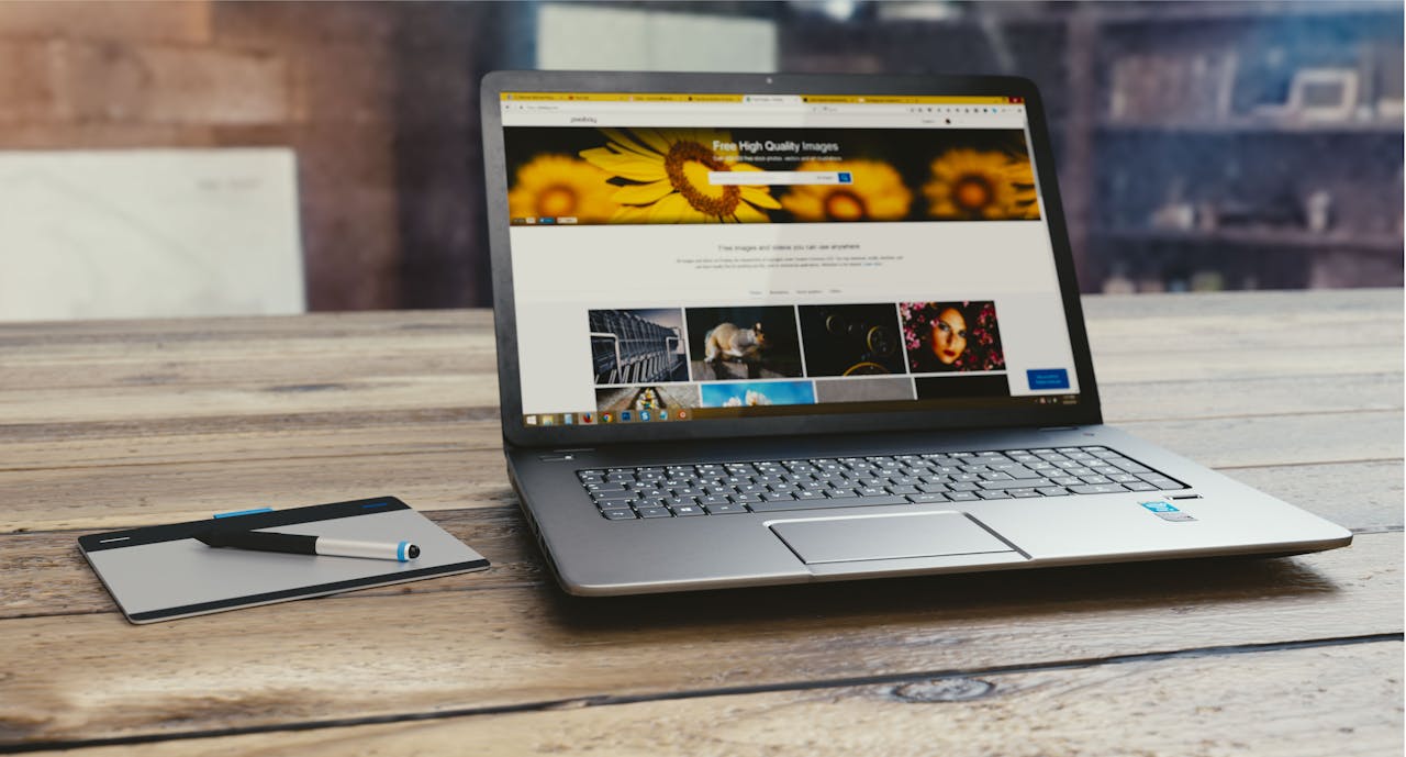 about-us-01 Laptop with open webpage on wooden desk, accompanied by tablet and pen, representing digital work setup.